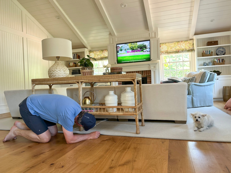 Man on hands and knees looking underneath family room table.
