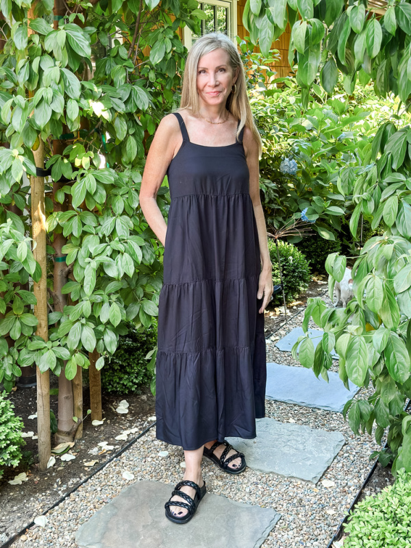 Woman in garden wearing black summer dress and sandals.