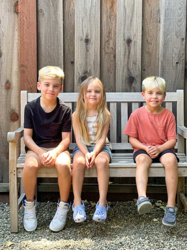Three children sitting on teak bench.