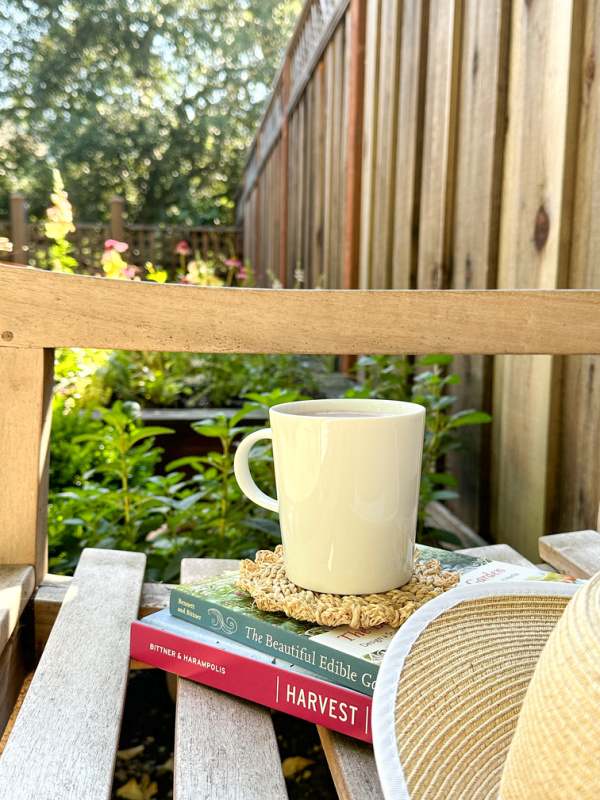 Gardening books and coffee cup sitting on teak bench in garden.