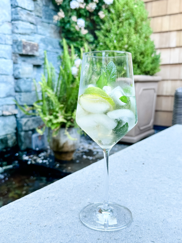 Glass of Hugo Spritz sitting on patio in front of water feature.