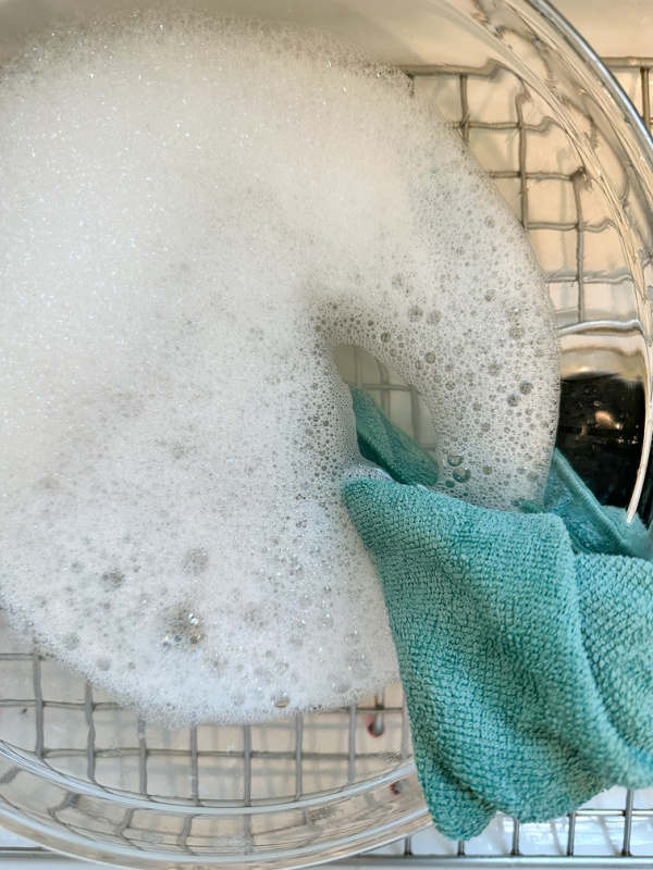 Bowl of soapy water and microfiber cloth in kitchen sink.