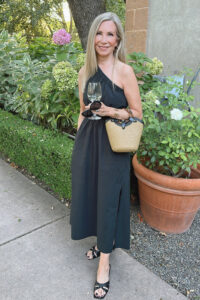 Woman in black one shoulder Rails dress holding glass of wine at Charles Krug Winery.