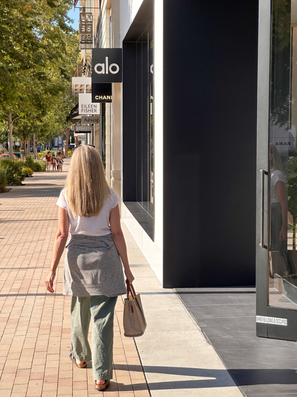 Woman walking down sidewalk of shopping mall in from of Alo Yoga.