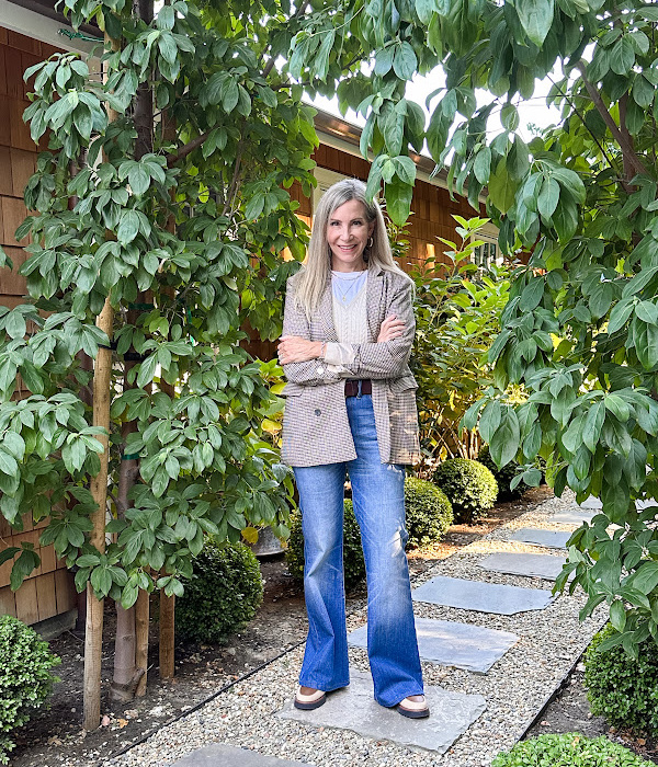 Woman standing in garden wearing jeans and a houndstooth jacket.