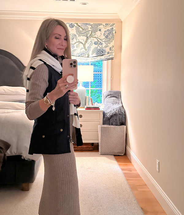 Woman taking mirror selfie swearing sweater dress, quilted vest and striped sweater.