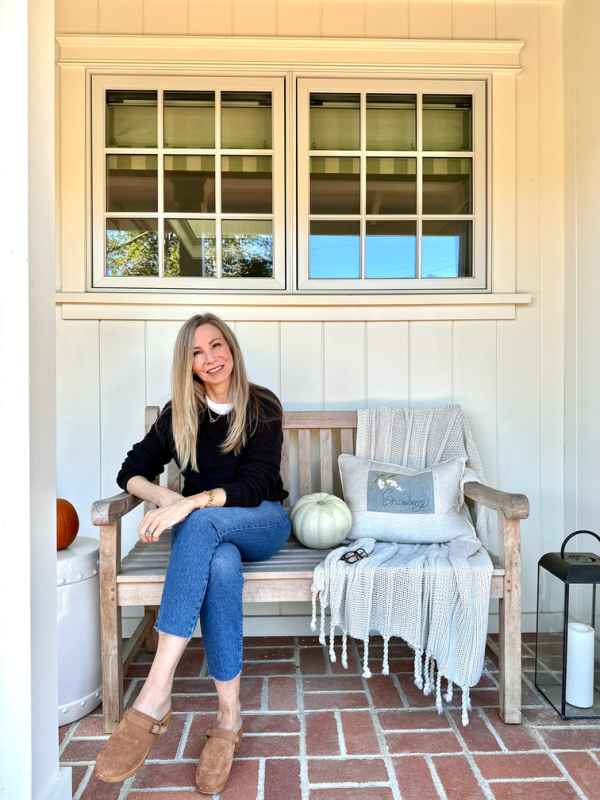 Woman sitting on porch bench next to pumpkins.