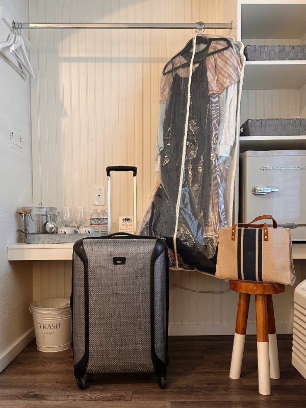 Hotel closet area with suitcase and purse on stool.