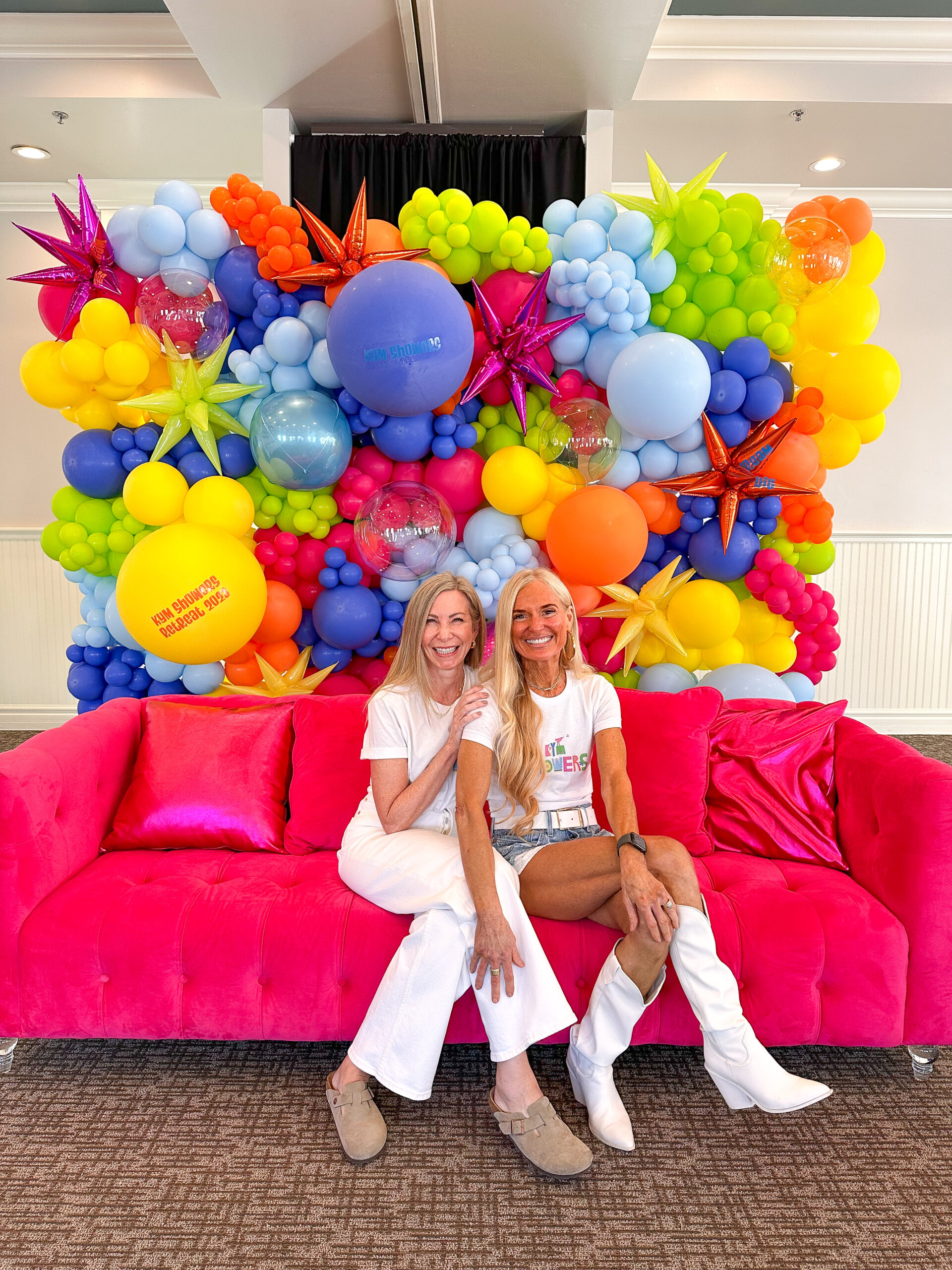 Two women sitting on bright pink sofa at Kym Showers Life Coach Retreat.