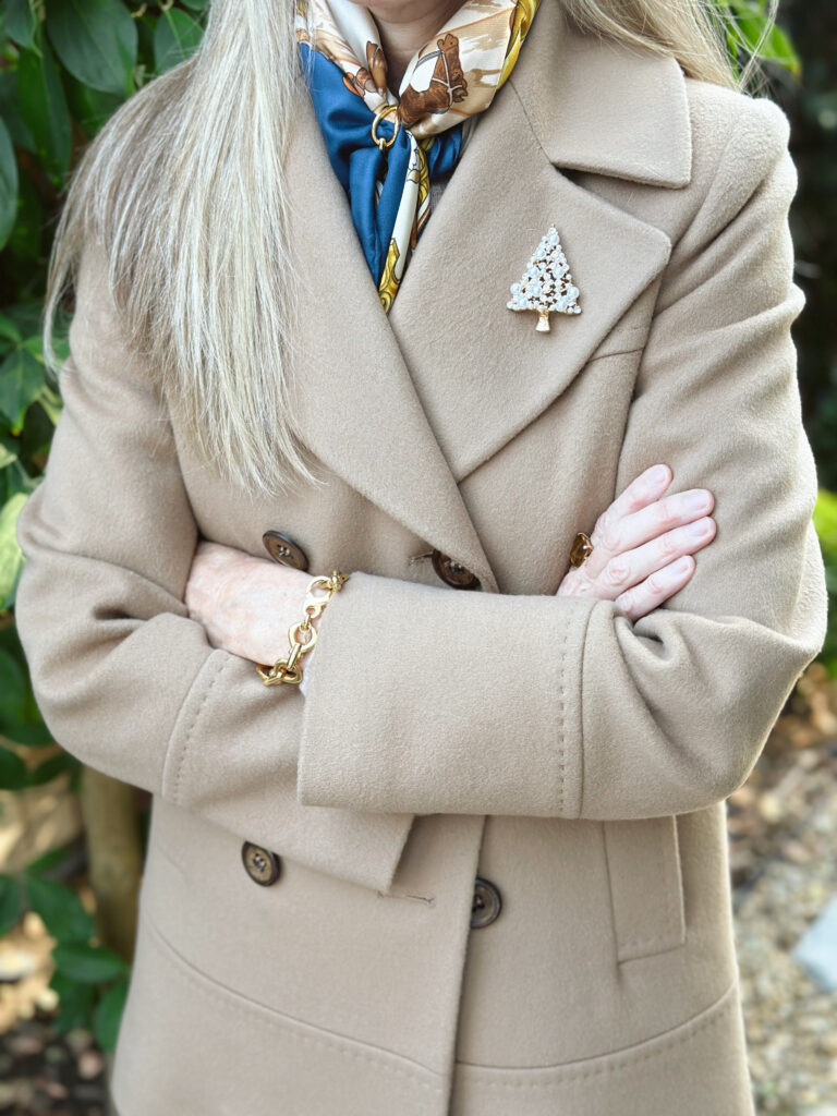 Woman wearing camel coat with Christmas tree brooch.