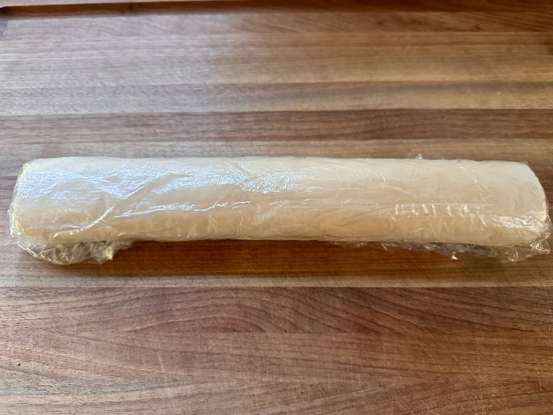Tube of wrapped cookie dough on cutting board.