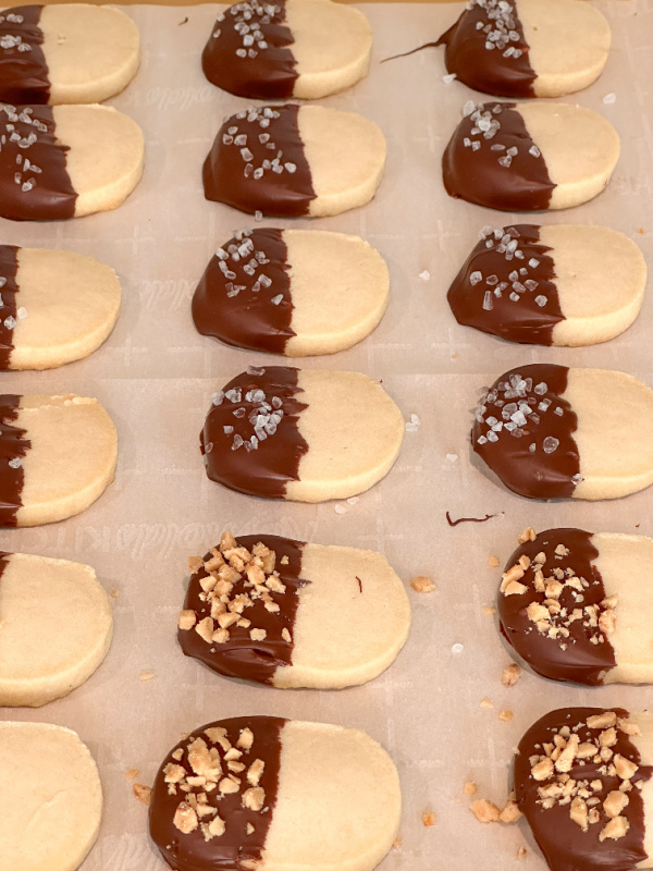 Shortbread cookies, half dipped in chocolate and sprinkled with salt and toffee on a cookie sheet.