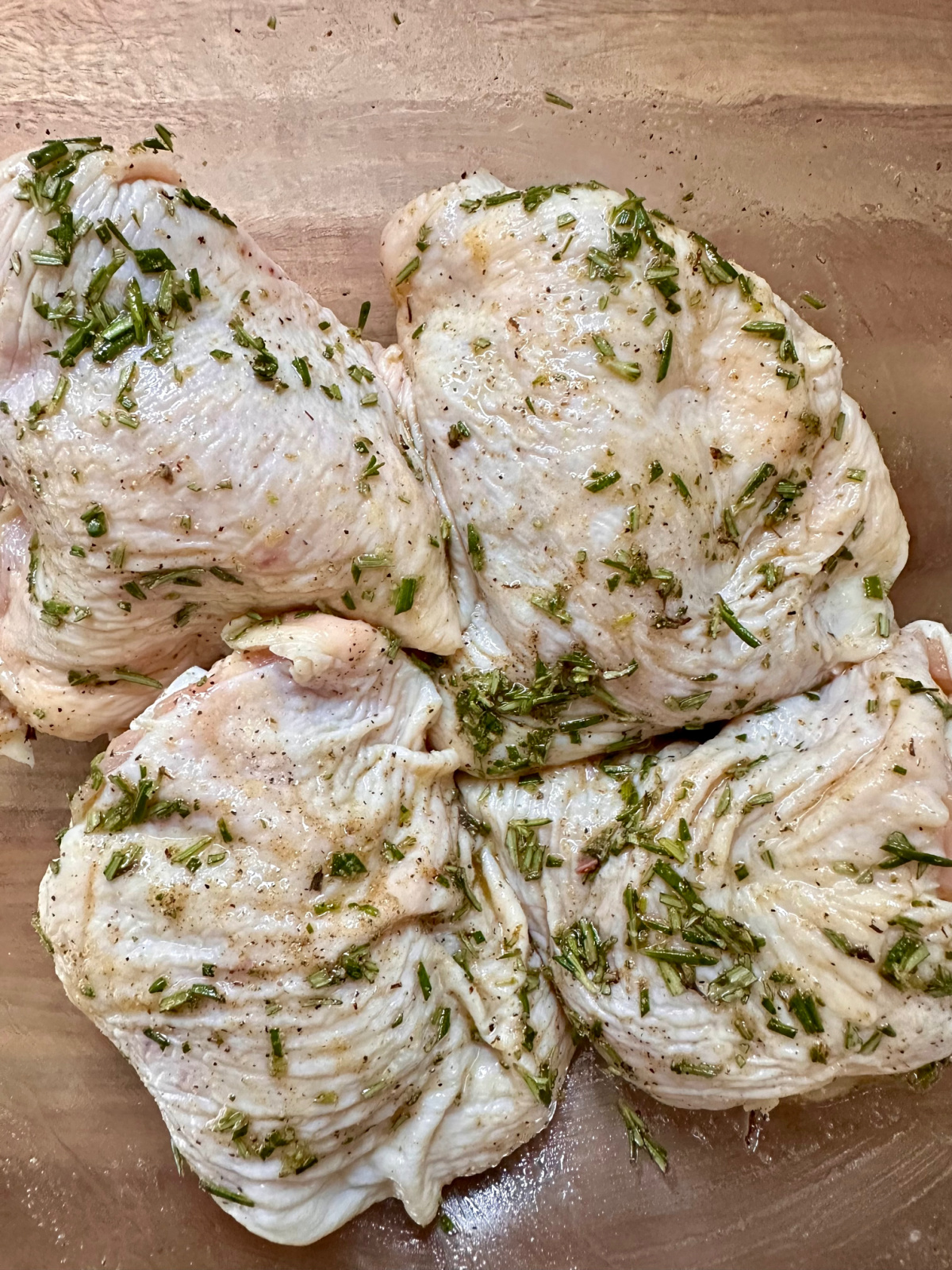 Chicken thighs marinating in olive oil and herbs.