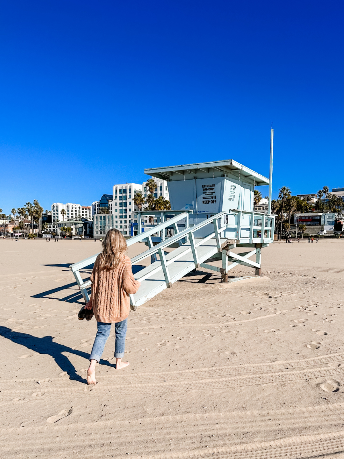 Woman walking on beach toward lifeguard tower.