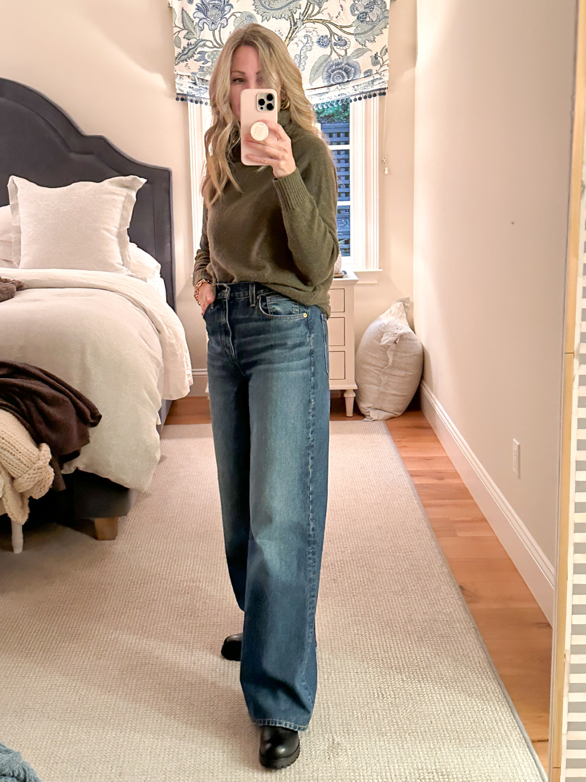 Woman wearing wide leg denim and a turtleneck sweater taking mirror selfie.