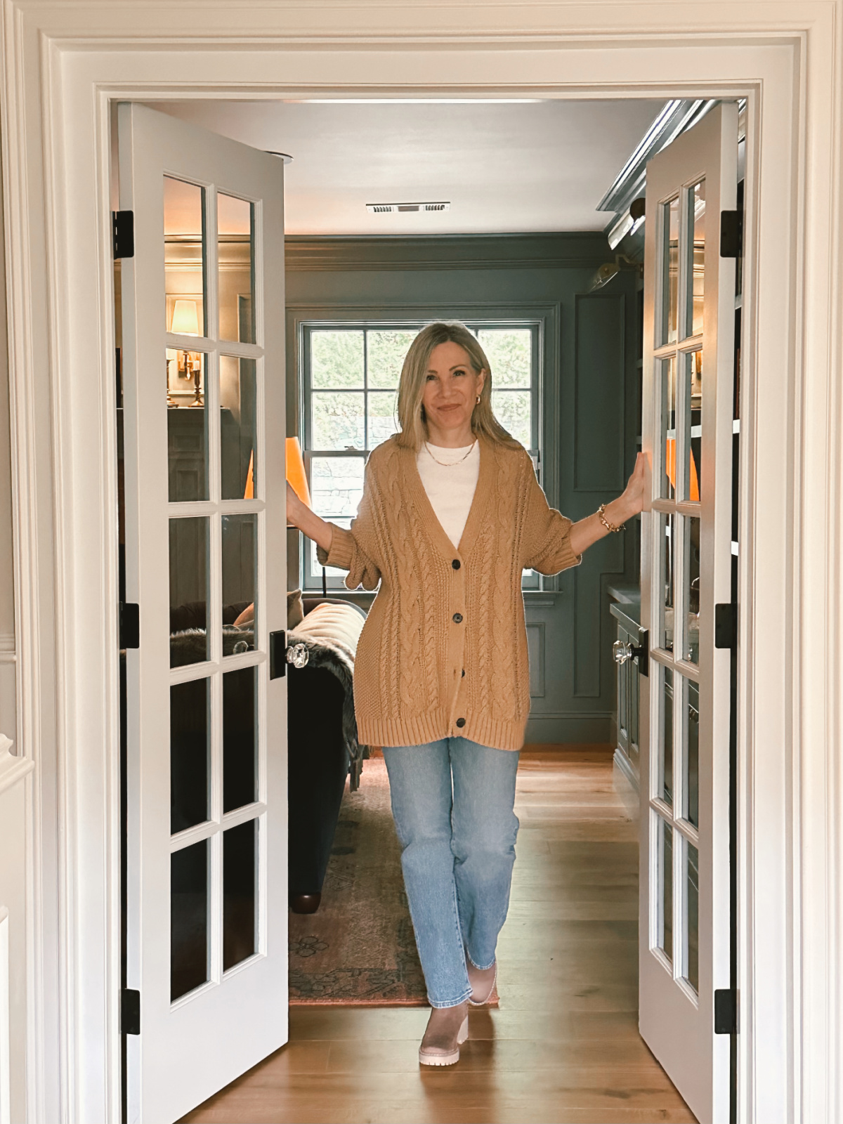 Woman standing in doorway wearing Quince cardigan and jeans.