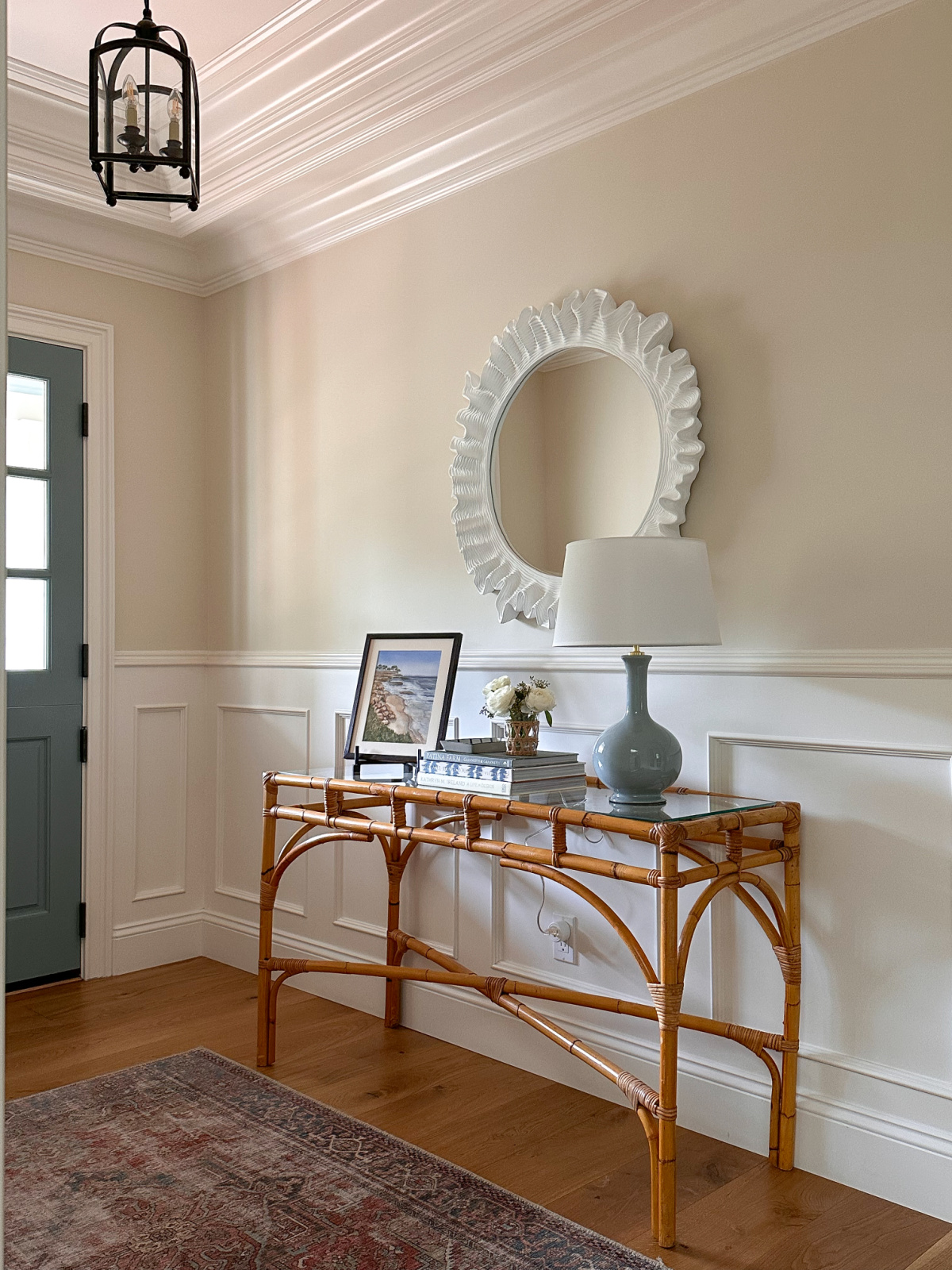 Entryway to house with bamboo console table and scalloped mirror.