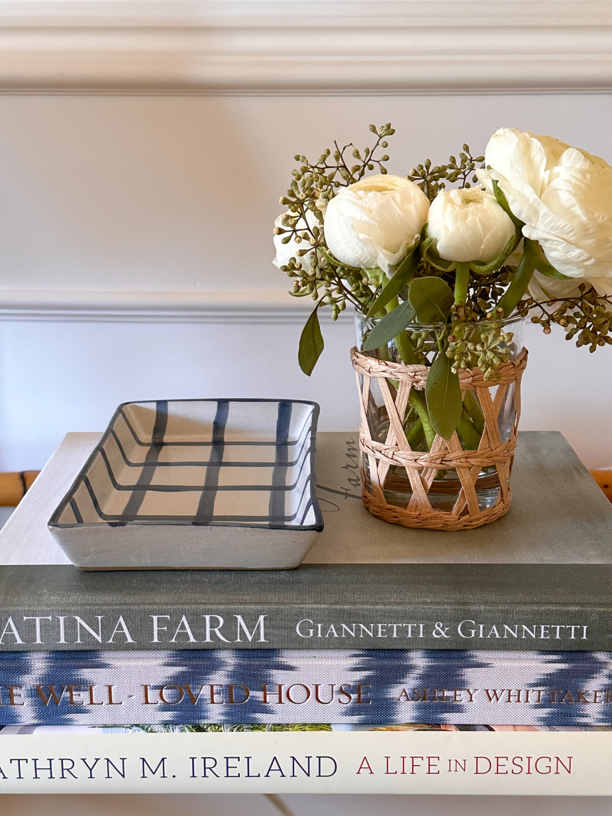 blue and white tray and woven flower vase sitting on books on entry table.