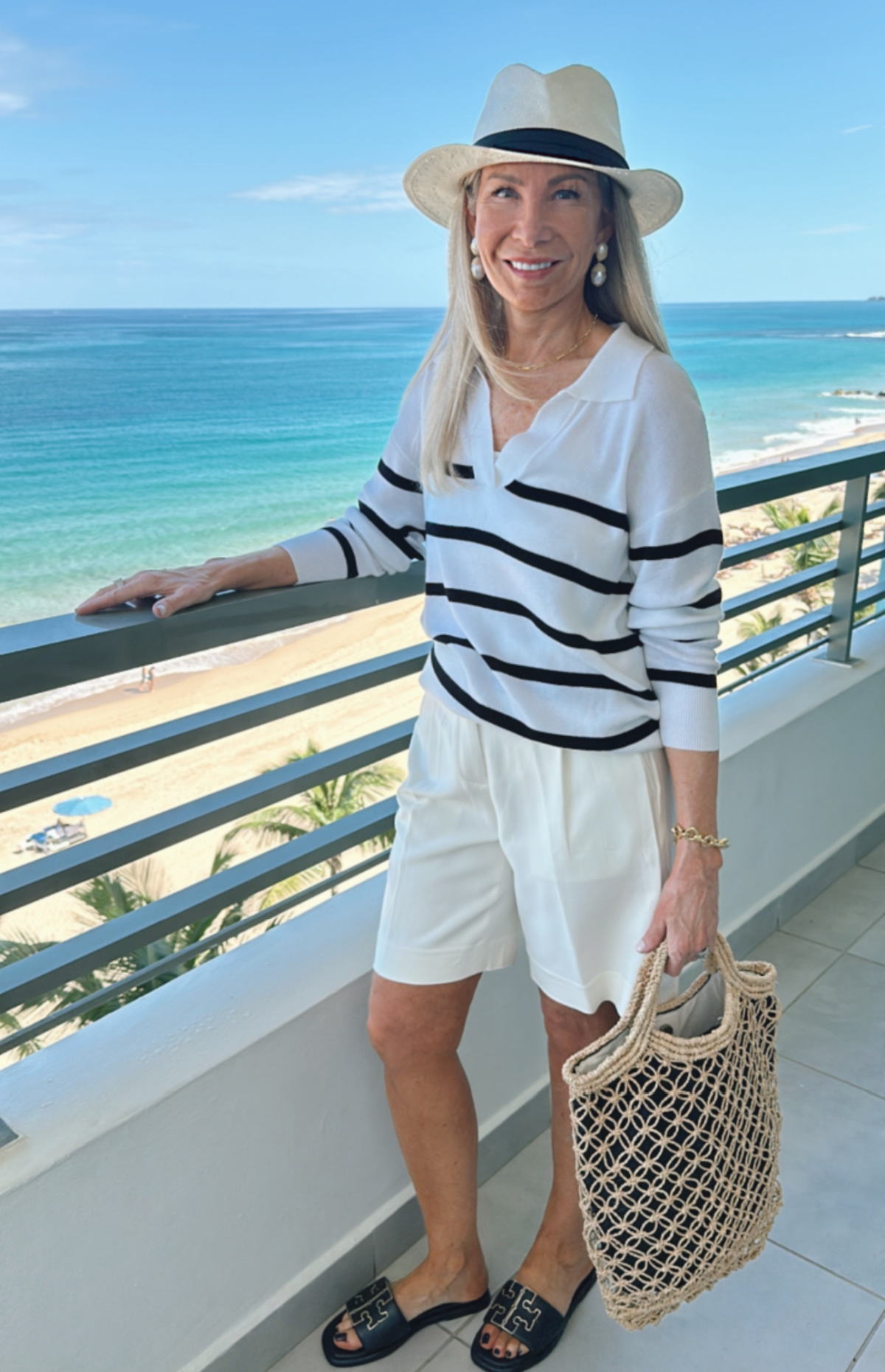 Woman standing on balcony overlooking Atlantic Ocean wearing striped sweater and ivory shorts.