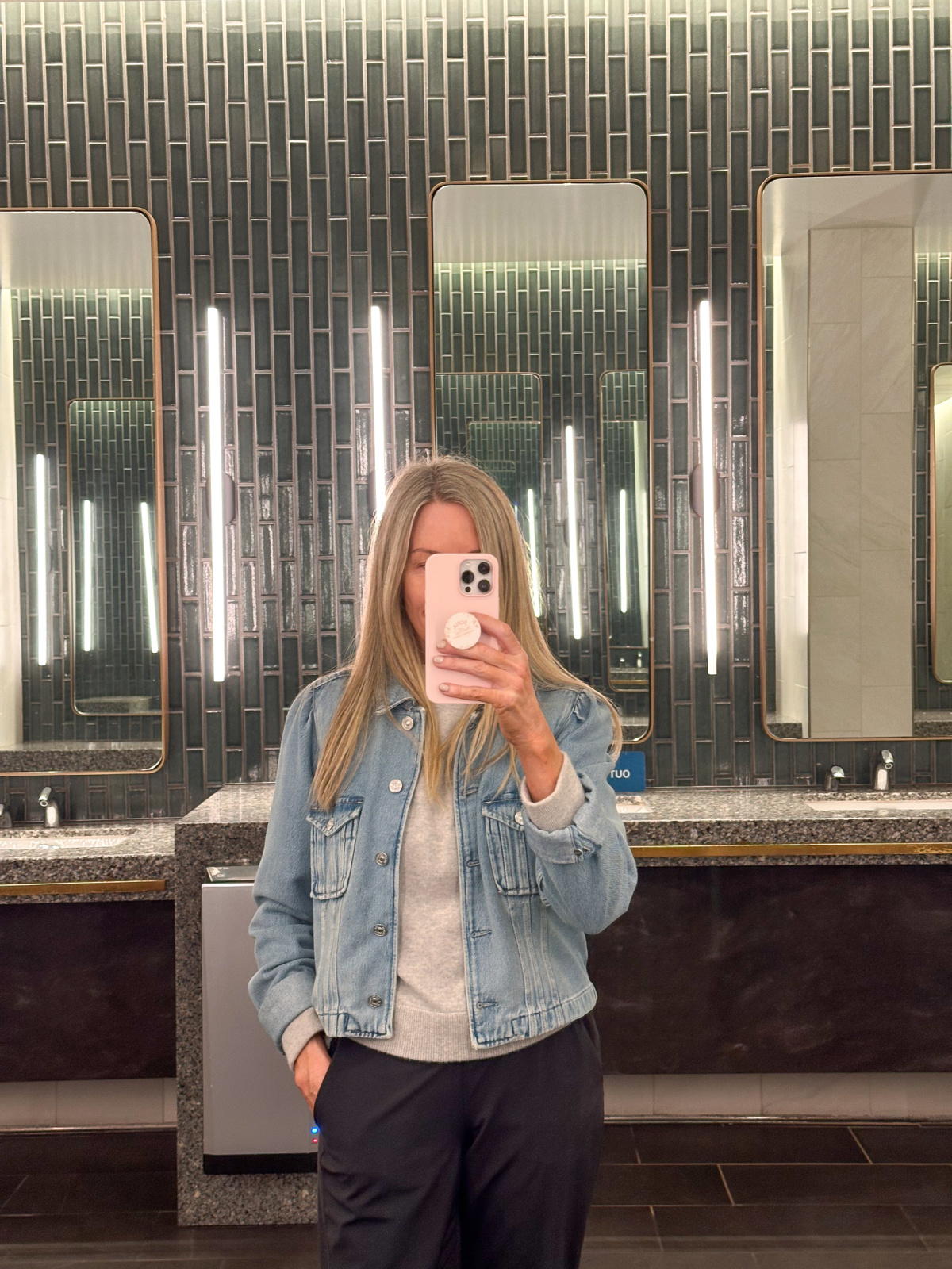 Woman taking mirror selfie in airport bathroom.