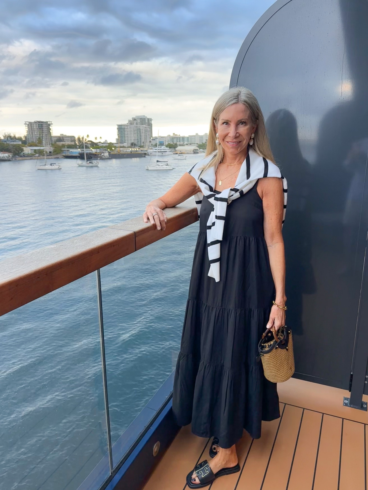 Woman wearing black dress and striped sweater on cruise ship deck.