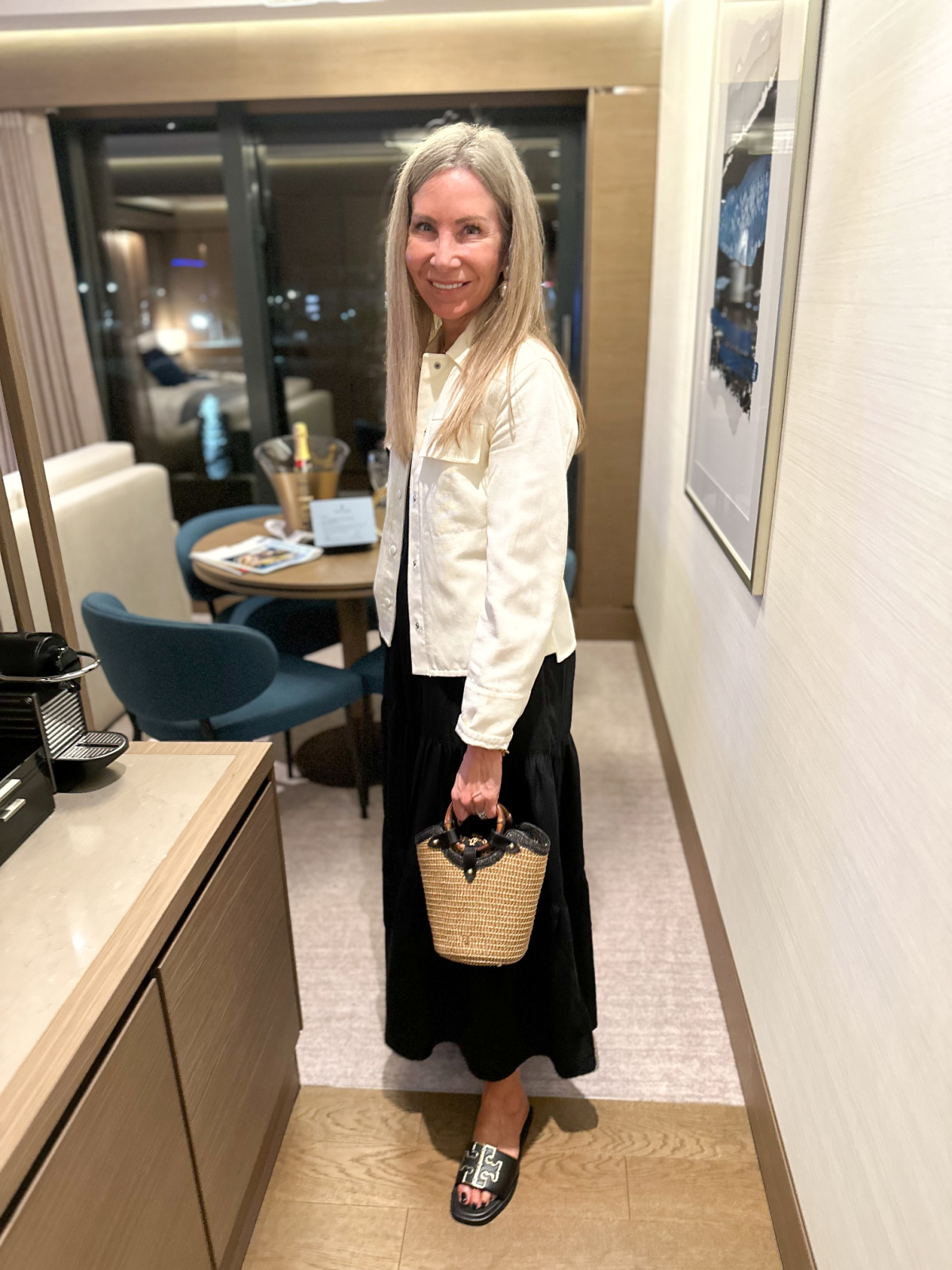 Woman wearing black dress and white jacket in cruise ship cabin.