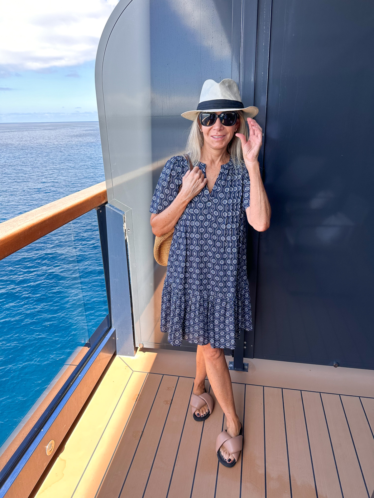 Woman standing on cruise ship terrace wearing Loft dress and sun hat.