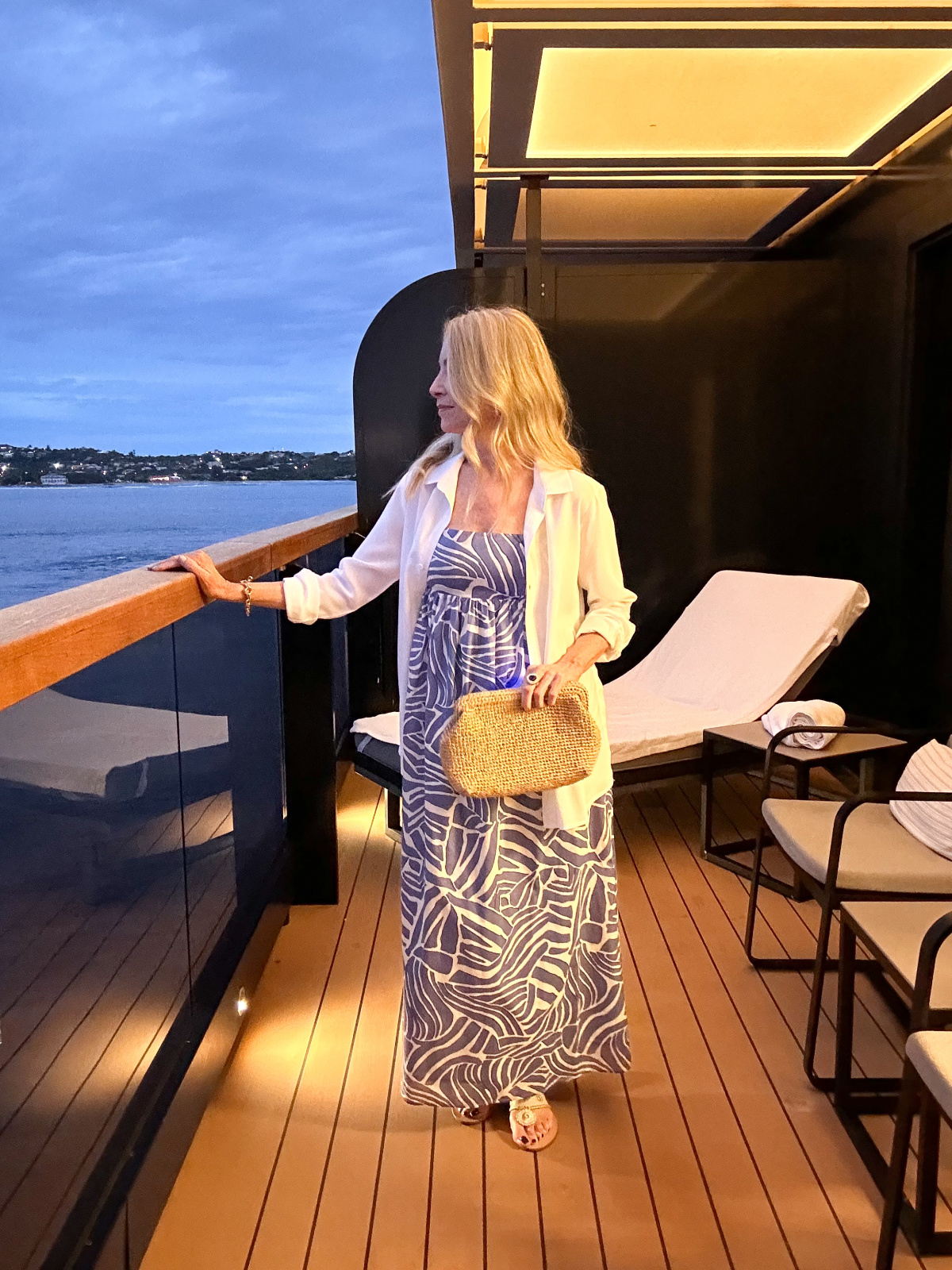 Woman wearing blue and white summer dress standing on cruise ship balcony.