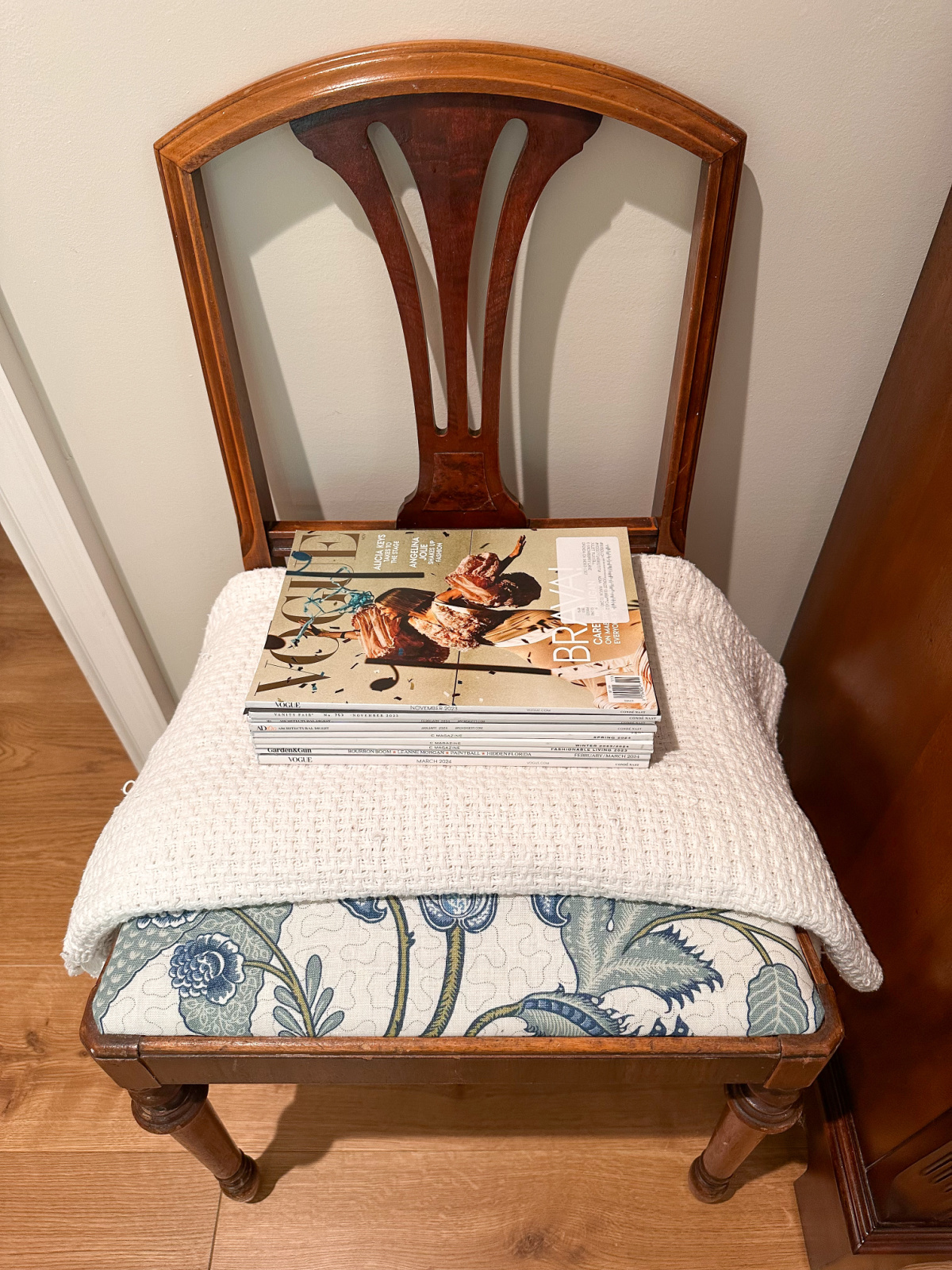 Old dining chair with throw blanket and magazines in seat.