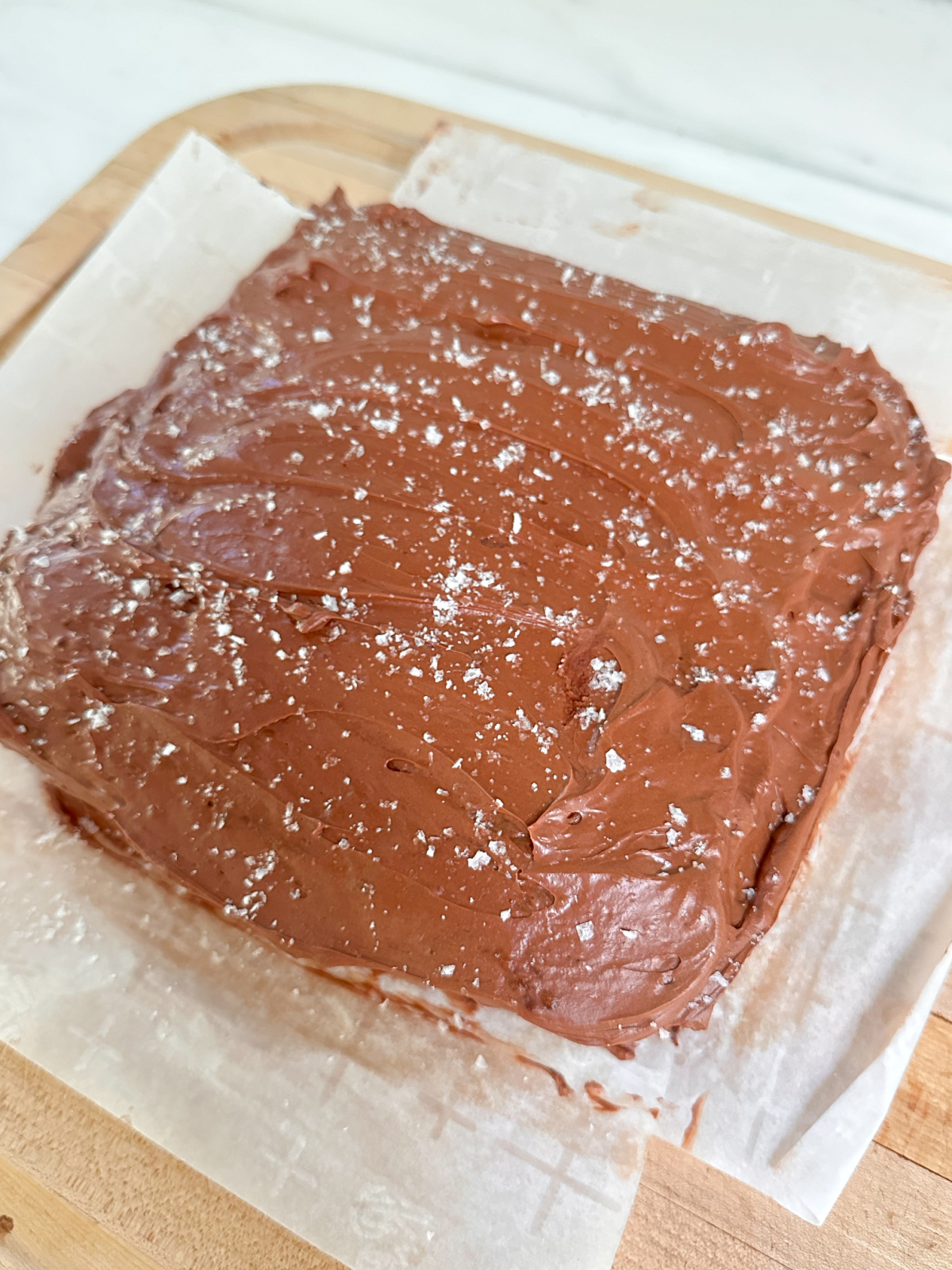 Banana cake with chocolate frosting and sea salt sitting on parchment sheets.