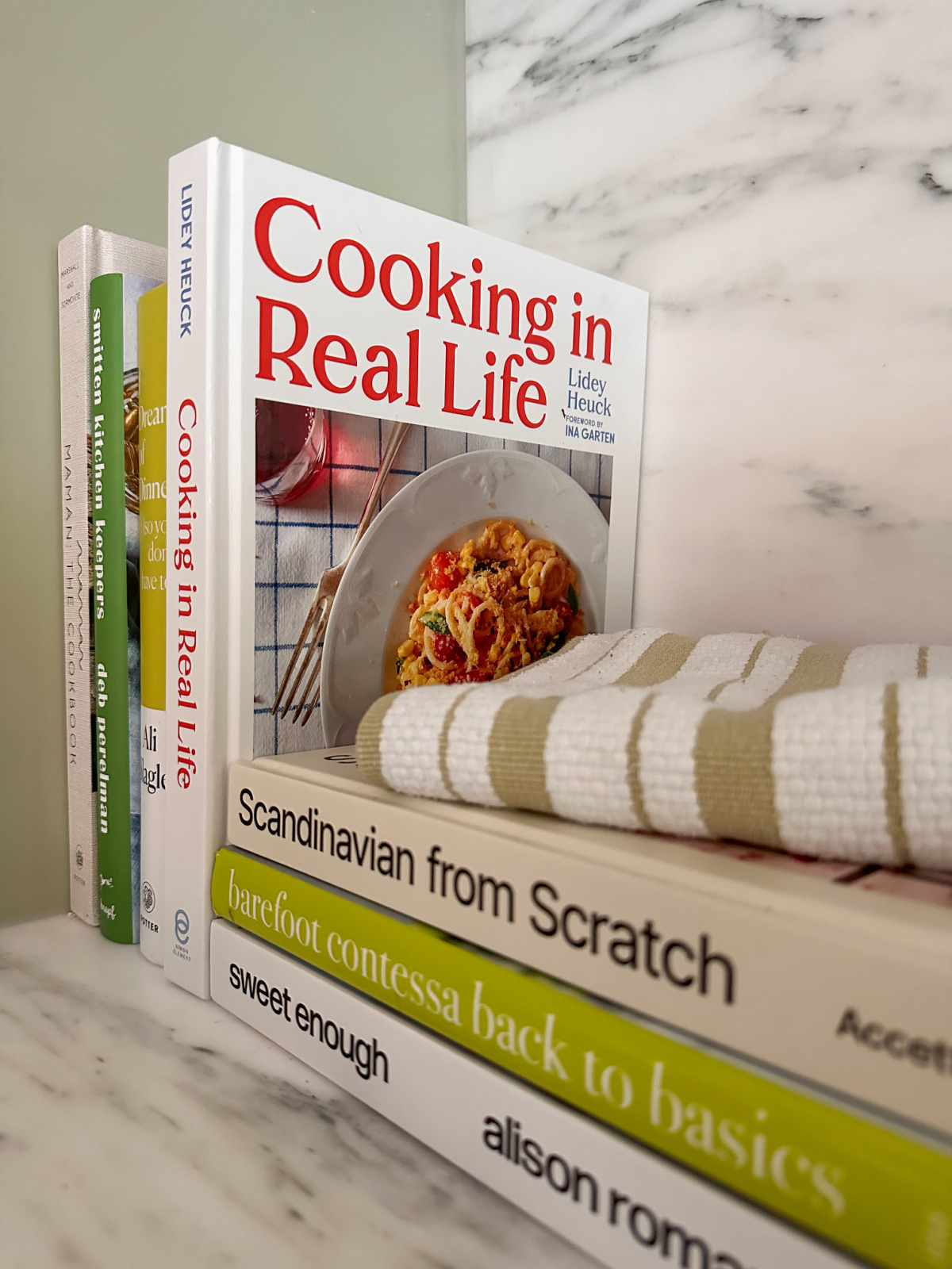Cookbooks stacked vertically and horizontally on kitchen countertop.