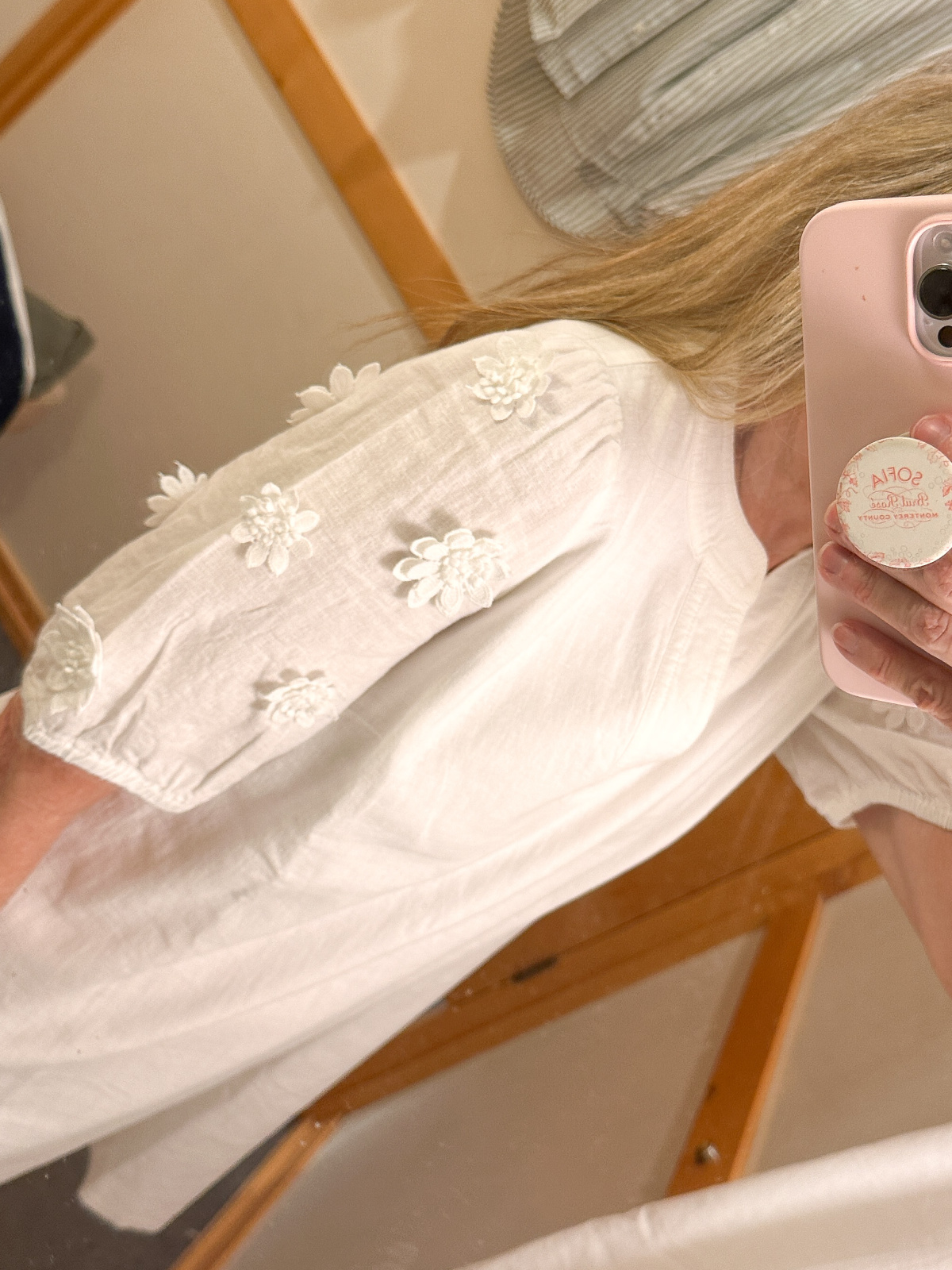 Woman taking mirror selfie of white blouse sleeve detail.