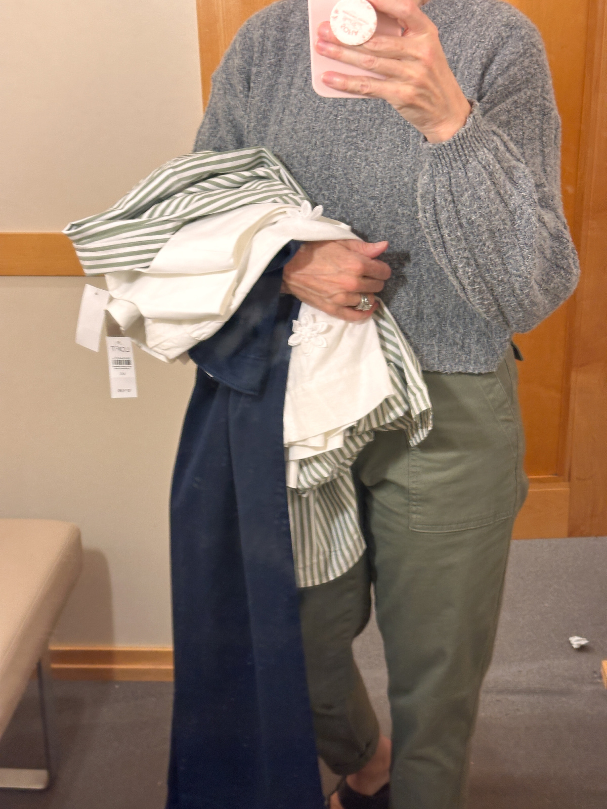 Woman standing in dressing room with several pieces of clothes over her arm.