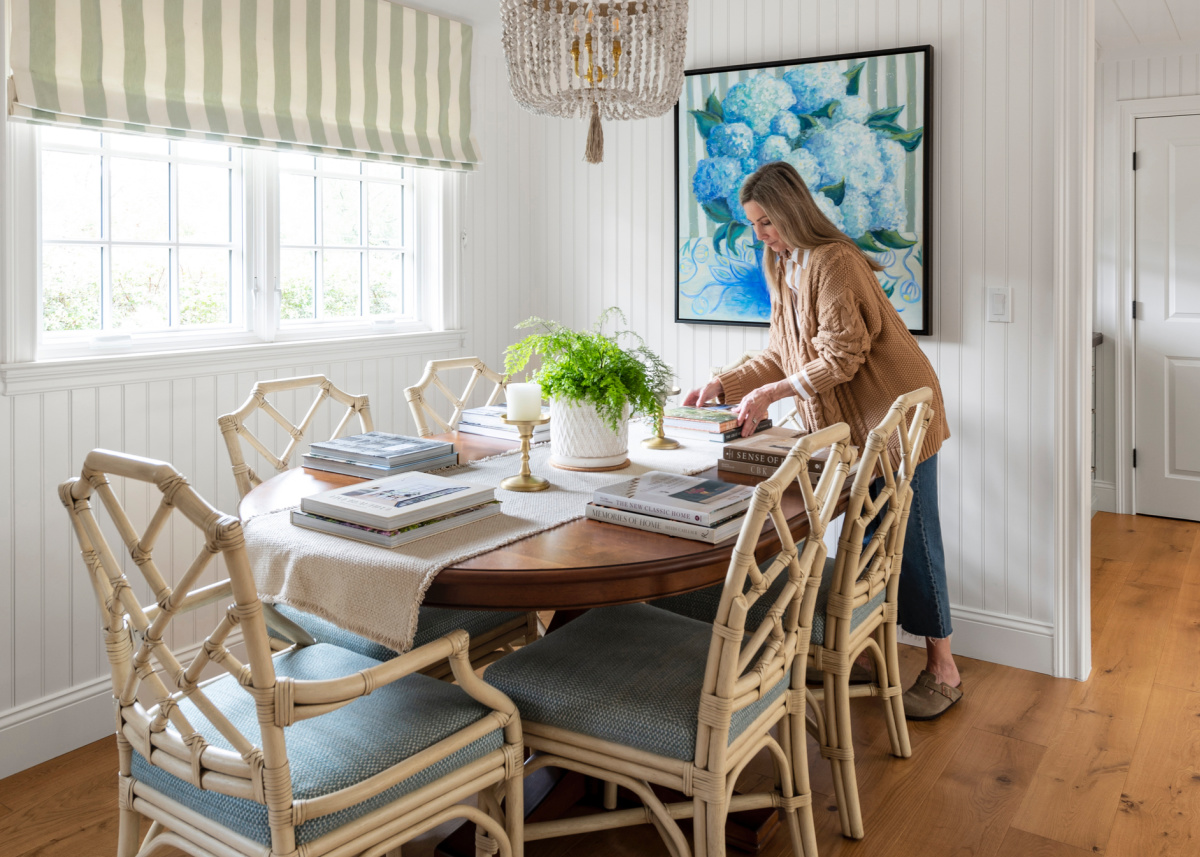 Woman setting dining table with large decor books.