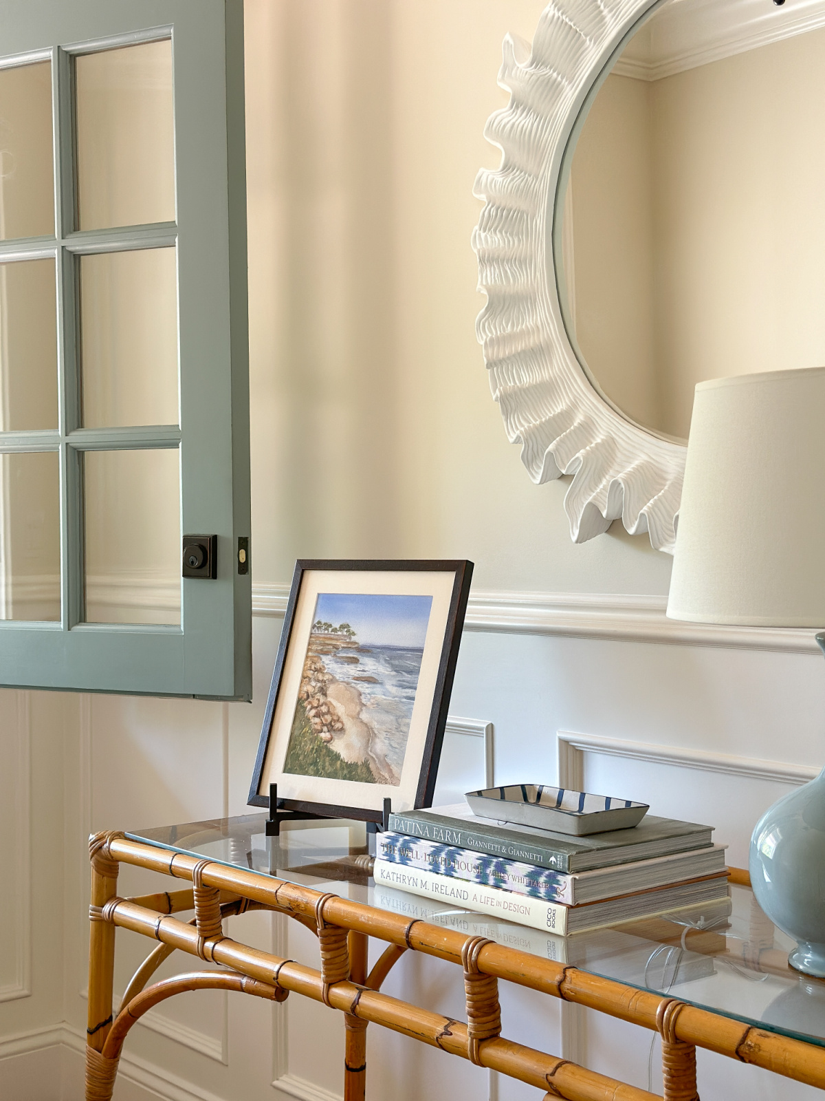 Open dutch door and entry console table with coastal art, books, lamp and round mirror.