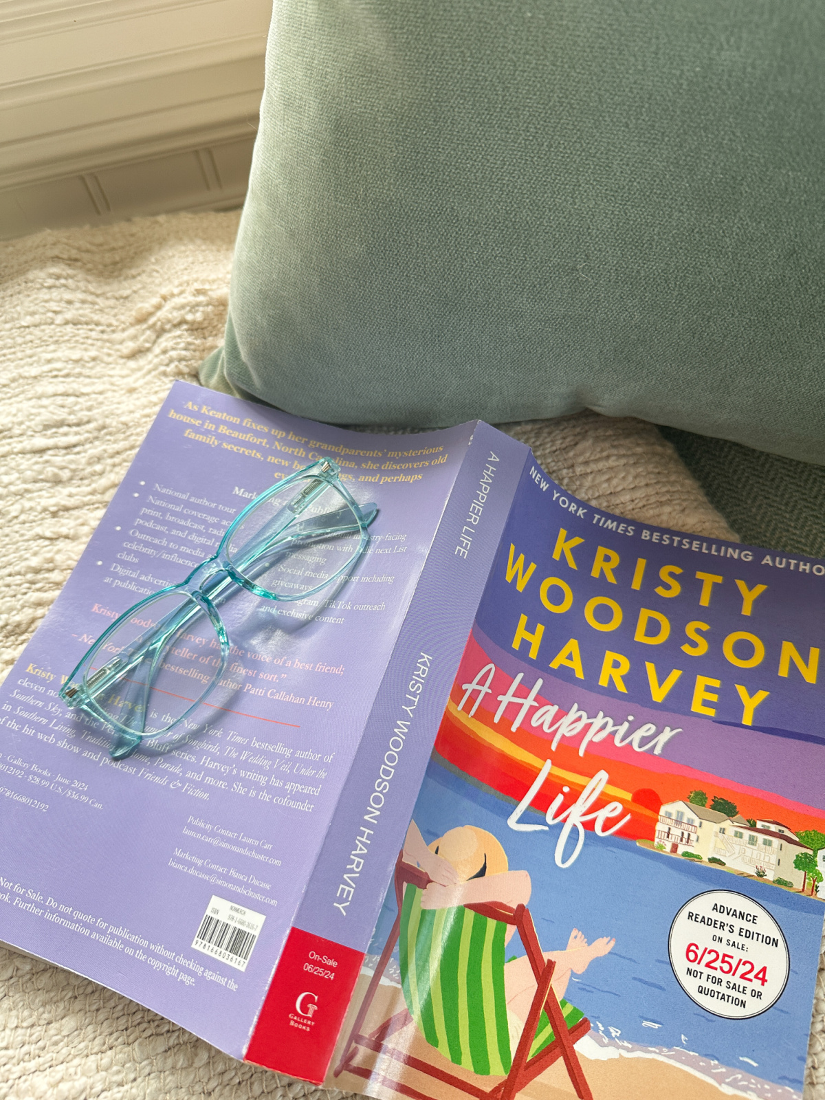 A Happier Life book open on bench next to pillow and a pair of reading glasses.