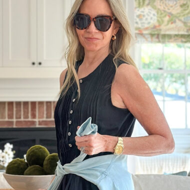 Woman wearing black Quince linen dress with blue shirt tied around waist and sunglasses.