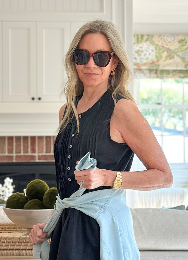 Woman wearing black Quince linen dress with blue shirt tied around waist and sunglasses.