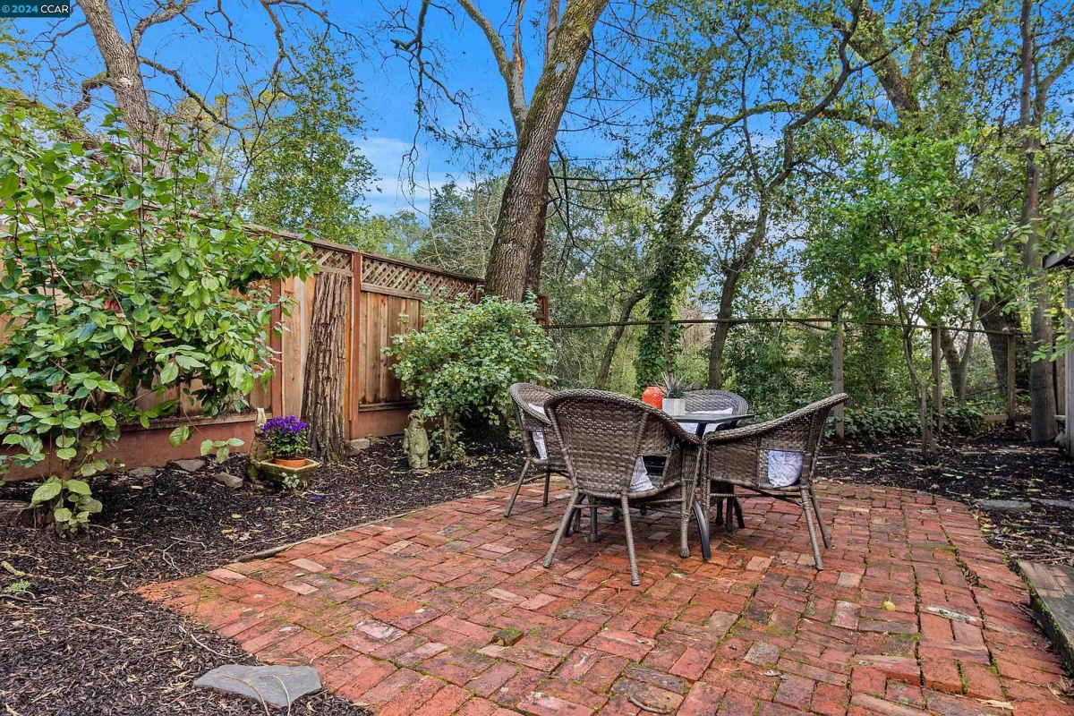 Wooded backyard with table and chairs on brick patio.