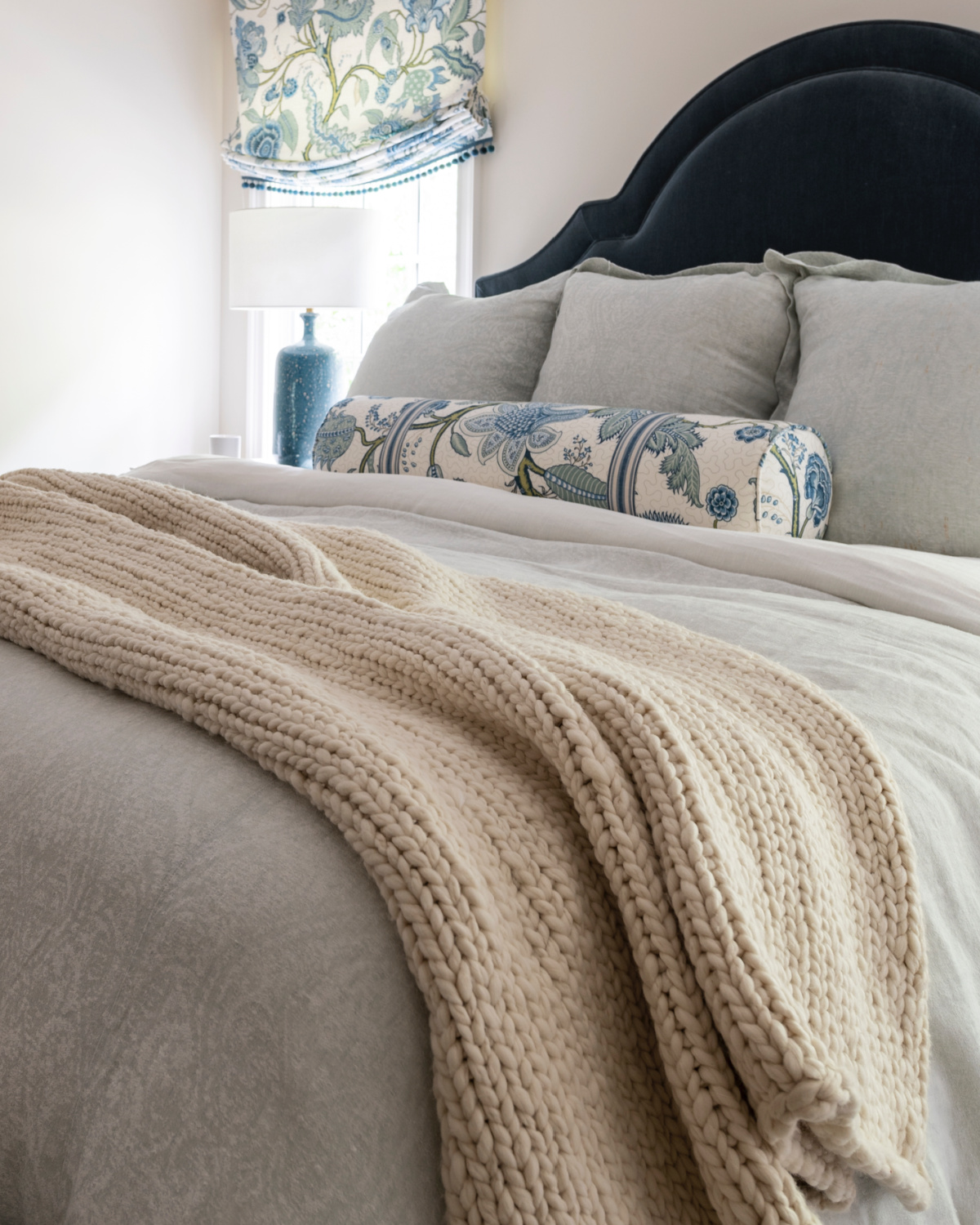 Bed with blue velvet headboard, linen duvet and chunky ivory throw blanket.