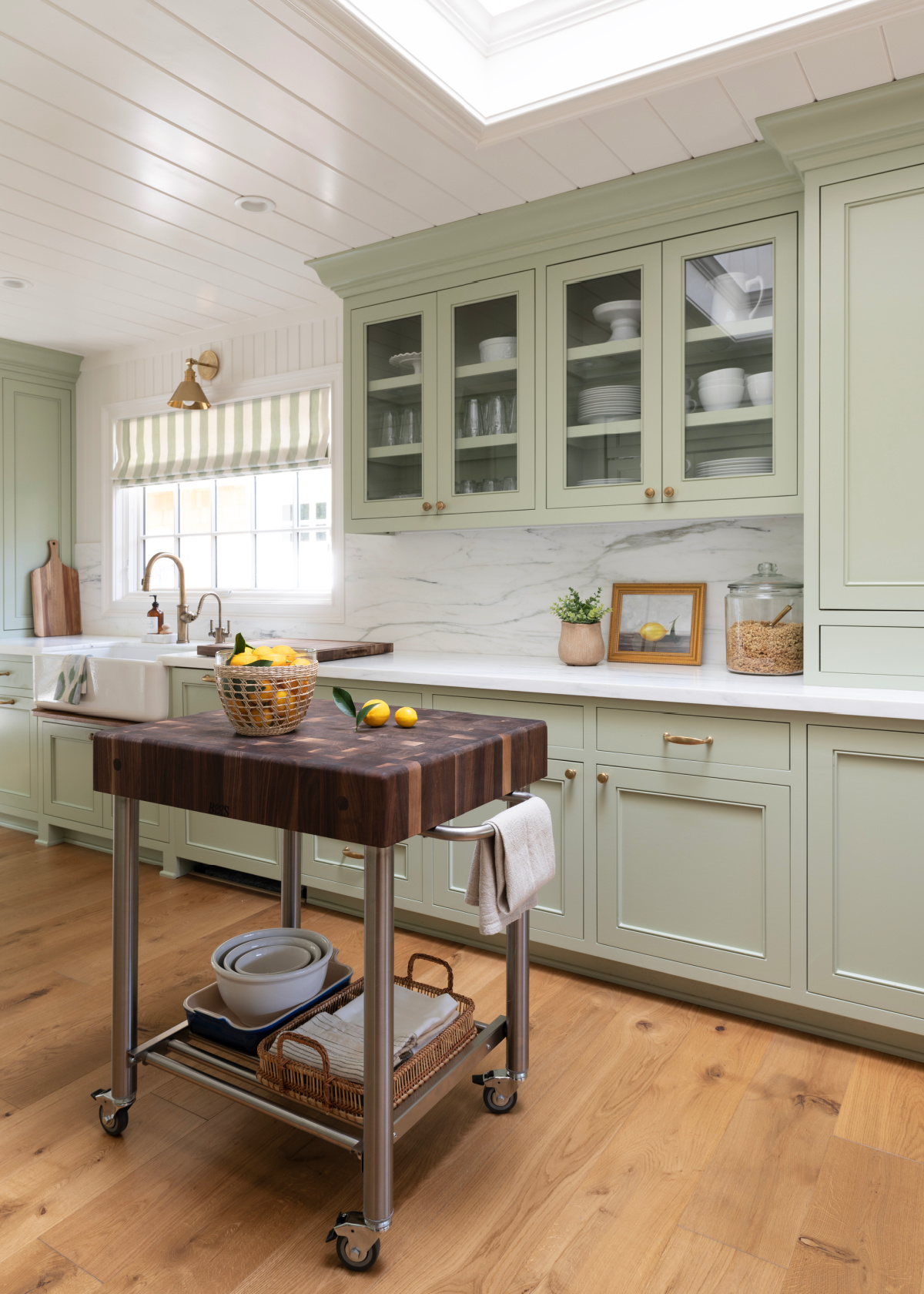 Butcher Block rolling island in kitchen with green cabinetry and glass front uppers.