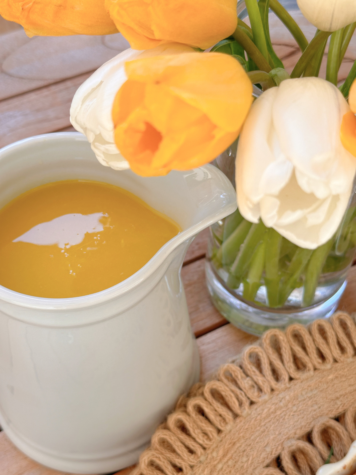 Pitcher of orange juice next to vase of yellow and white tulips.