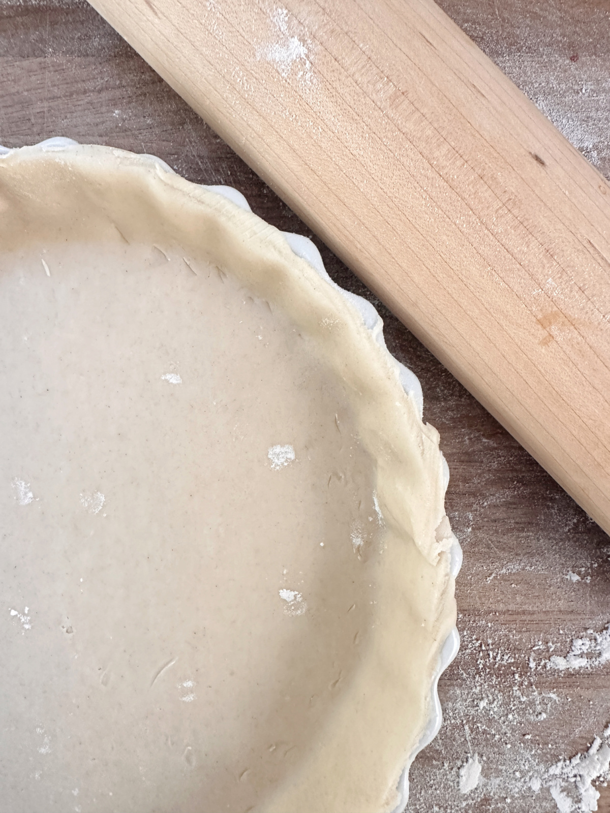 Overhead shot of pie crust in white pie plate next to rolling pin.