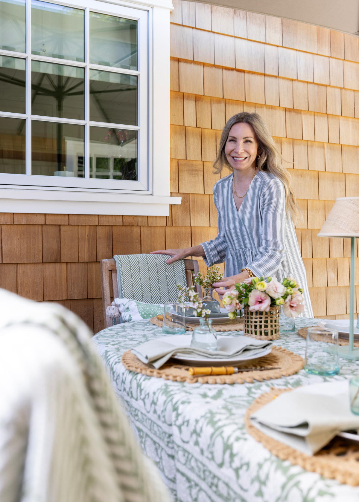 Woman standing behind outdoor dinner table.