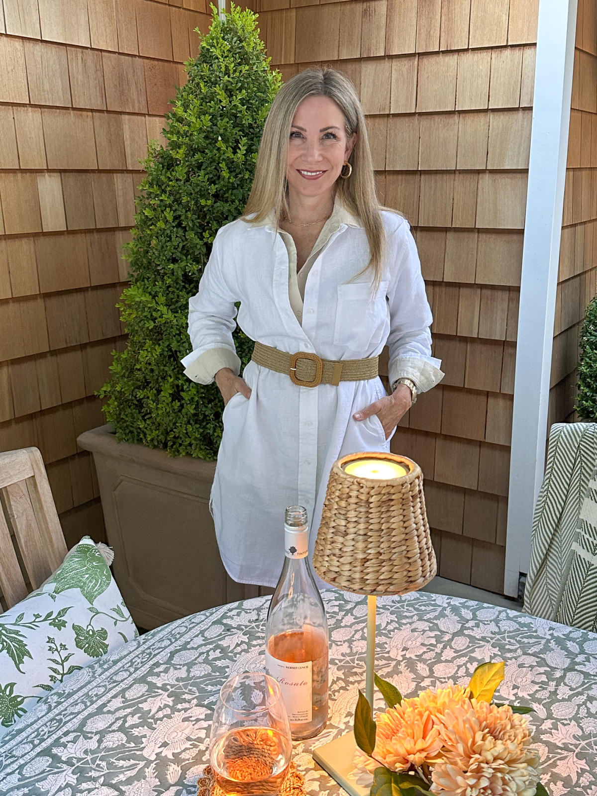 Woman standing behind patio table wearing white shirt dress.